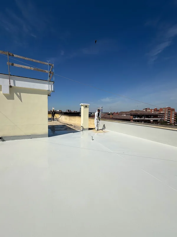 Operatore con attrezzatura a spruzzo al lavoro sulla copertura piana e lungo il parapetto.