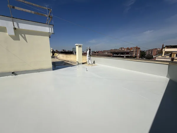 Lavorazione a spruzzo della copertura piana con tubazioni e operatori sullo sfondo.