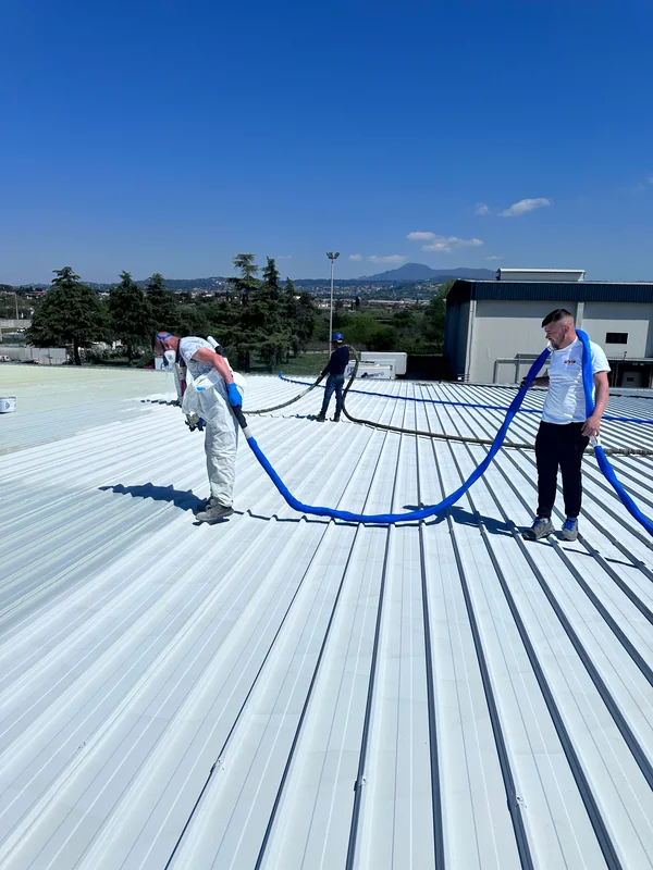 Operatori con attrezzatura a spruzzo e tubazioni blu su copertura industriale in lamiera grecata.