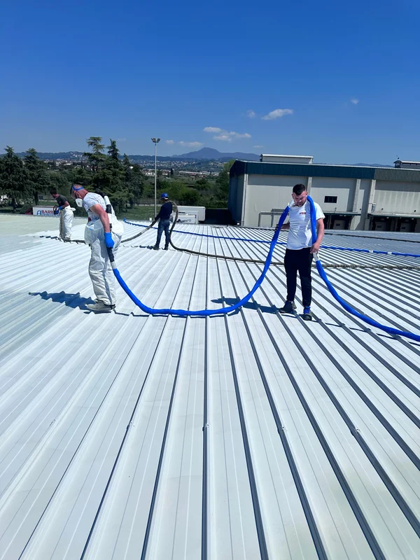 Squadra operativa su copertura industriale, con attrezzatura a spruzzo e tubazioni di alimentazione.