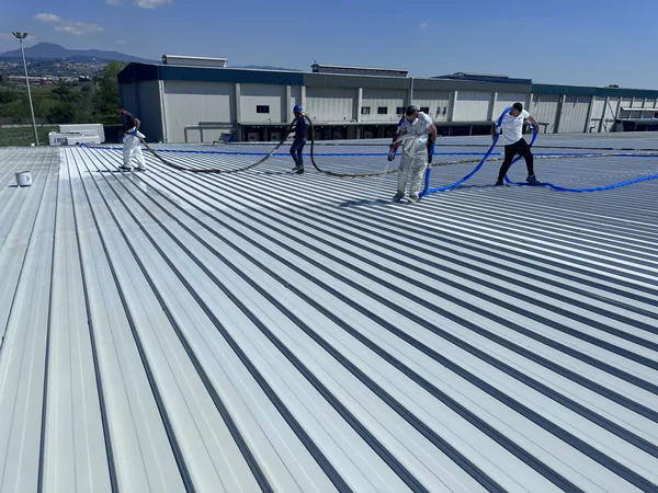 Quattro operatori distribuiti su una copertura industriale durante la lavorazione a spruzzo.