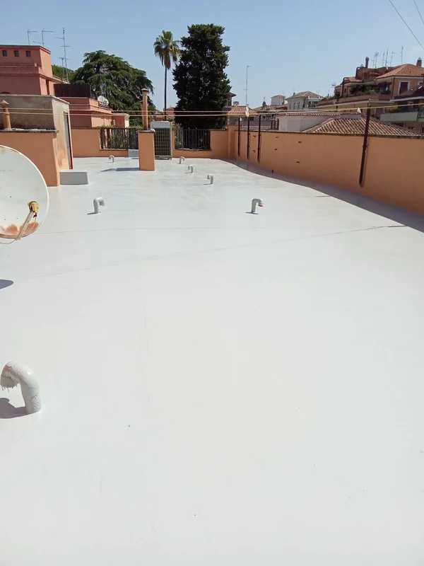 Superficie chiara della copertura piana con raccordi alle tubazioni emergenti, parapetti e antenne.