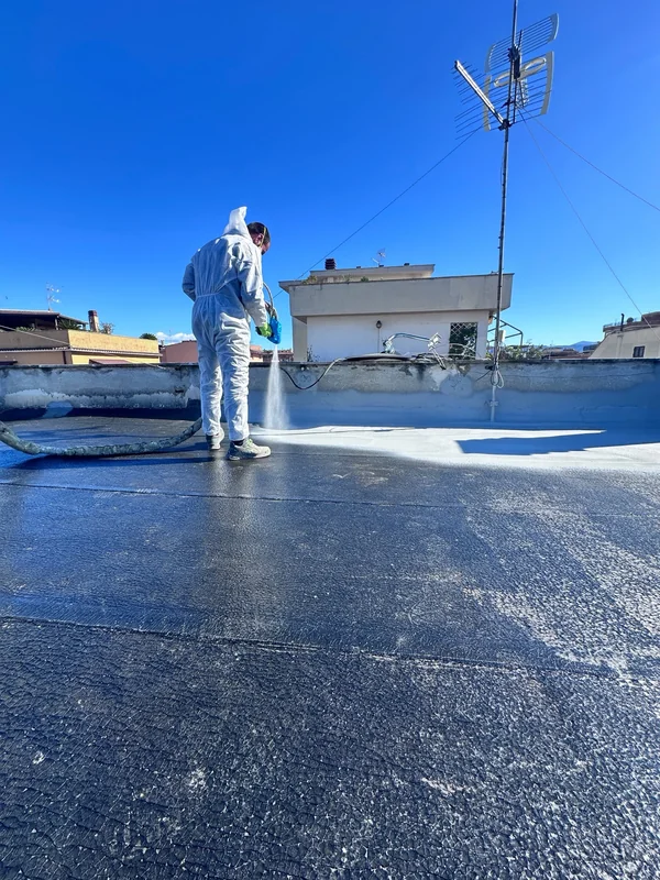 Operatore con attrezzatura a spruzzo durante la posa del rivestimento chiaro sulla superficie scura della copertura.