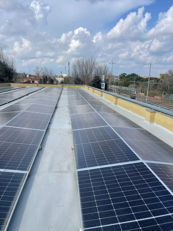 Superficie chiara e raccordi perimetrali della copertura tra le file di pannelli fotovoltaici.