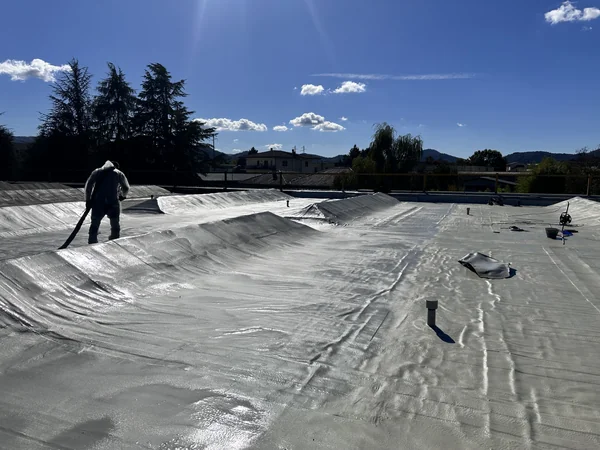 Operatore sulla copertura con rivestimento chiaro, tubazioni emergenti e zona scura sul perimetro.