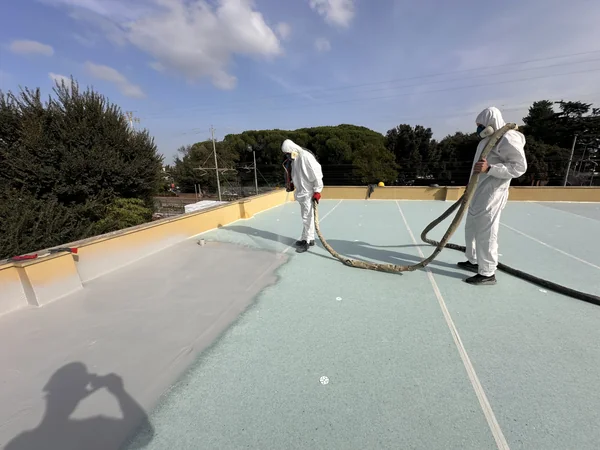 Operatori con attrezzatura a spruzzo sulla copertura, vicino alle fasce di raccordo perimetrali.
