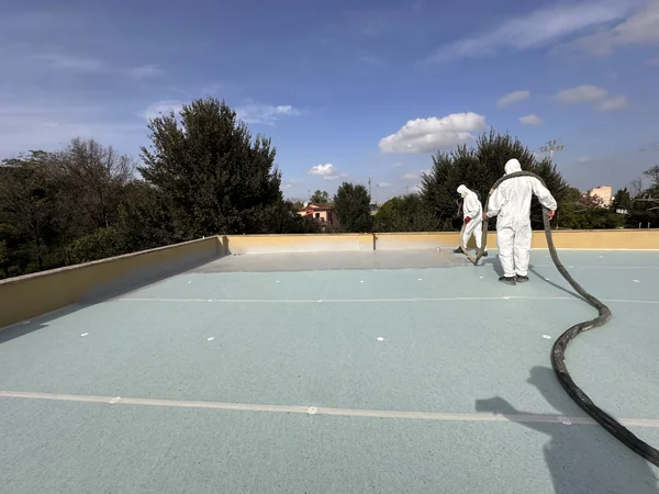 Applicazione del rivestimento sulla copertura, con operatori e tubazioni di alimentazione.