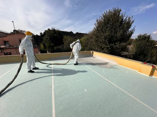 Due operatori con tubazione di alimentazione durante la lavorazione a spruzzo sulla copertura.