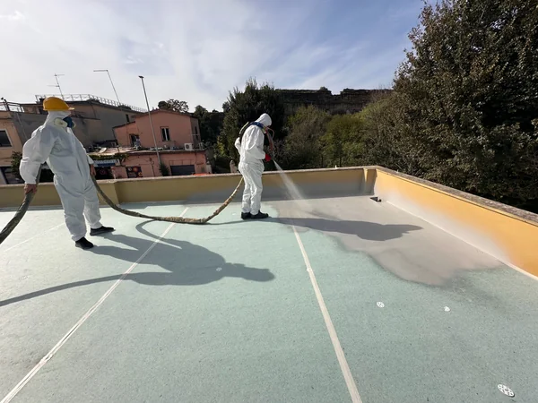 Operatore e assistente sulla copertura durante l’applicazione del rivestimento a spruzzo.