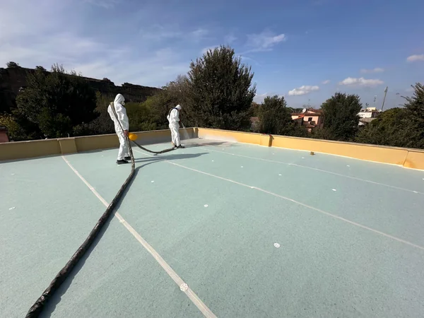 Due operatori durante l’applicazione a spruzzo, con giunti visibili e parapetti sullo sfondo.