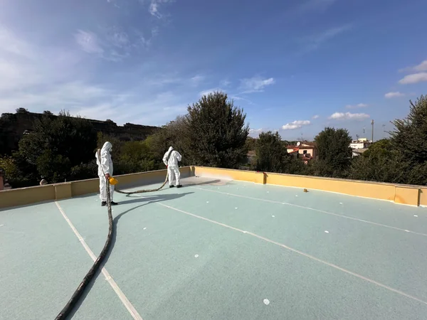 Due operatori durante la posa a spruzzo sulla superficie della copertura, con zone di rivestimento diverso.